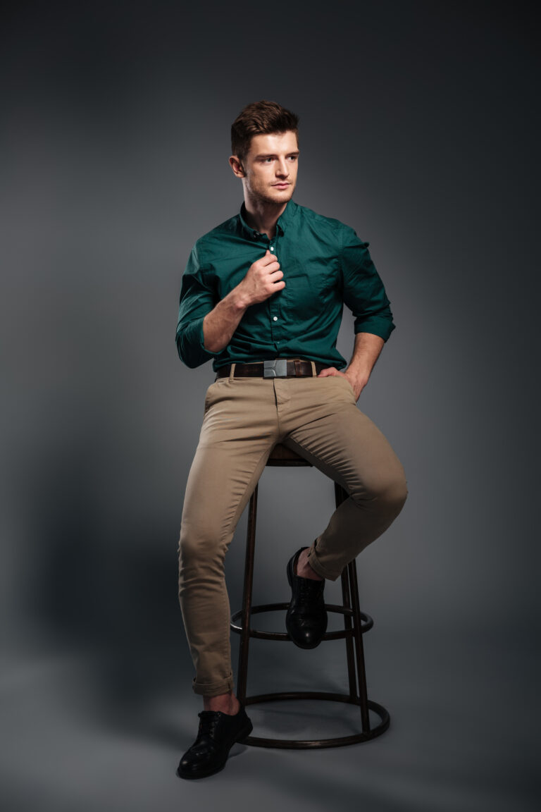 Image of serious handsome young man sitting isolated over grey background. Looking aside.