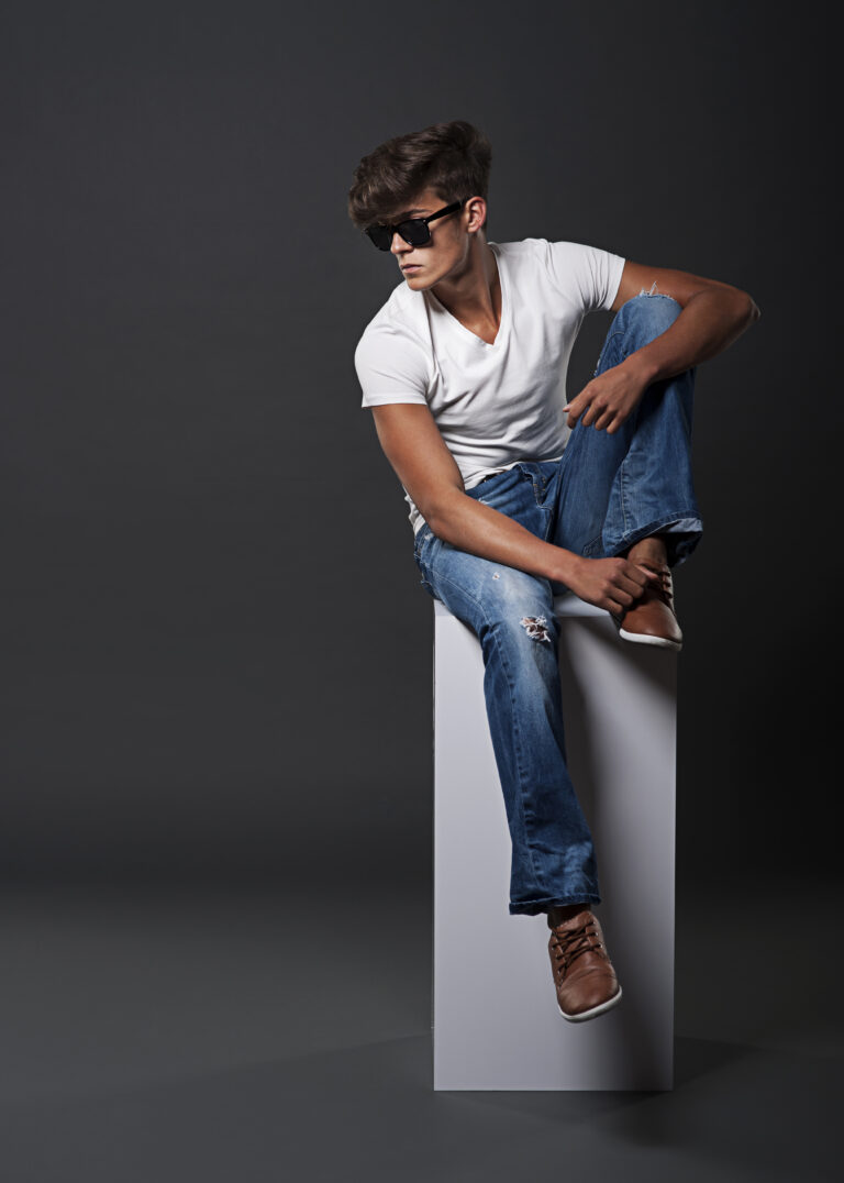 Young fashion man sitting on white rectangle